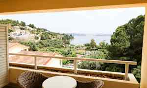 Udsigt fra en altan over grønne områder, bygninger og en bugt. (AI-genereret tekst)