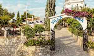 En stenlagt indgang til Villa Nina med blomster og grønne omgivelser. (AI-genereret tekst)