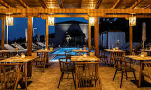 Udendørs servering med træstole og borde, pool og belysning om aftenen. (AI-genereret tekst)