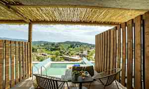 Terrasse med trævægge, bord og stole, pool og udsigt over landskab med huse og grønne bakker. (AI-genereret tekst)