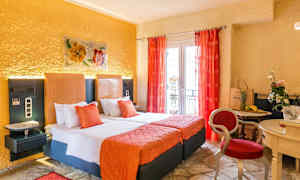 Et hotelværelse med to senge, orange indretning og røde gardiner samt et mindre bord med stole og dekorationer. (AI-genereret tekst)