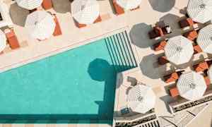 En pool med turkis vand omgivet af liggestole under stribede parasoller. (AI-genereret tekst)