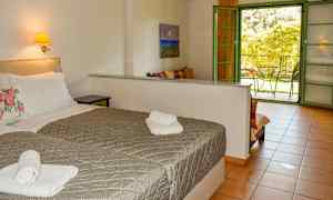 Hotelværelse med to senge, et belyst vægmonteret natbord og en åben dør til en balkon. (AI-genereret tekst)