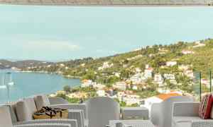 Udendørsmøbler på en terrasse med udsigt over havet og en kystby. (AI-genereret tekst)