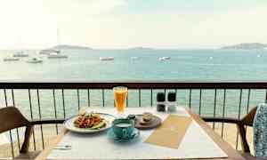 Udsigt over en tallerken med mad og en kop kaffe placeret på et bord på en altan med havudsigt. (AI-genereret tekst)