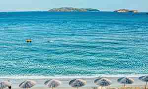 Strand med parasoller, hav og øer i baggrunden. (AI-genereret tekst)