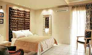 Et soveværelse med en dobbeltseng, en stor polstret sengegavl og et spejl på væggen. (AI-genereret tekst)