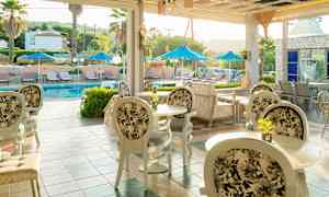 Billede af en udendørs servering med borde og stole, samt en pool med liggestole og parasoller i baggrunden. (AI-genereret tekst)