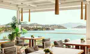 Udendørs servering med borde og stole samt udsigt over havet og frodige øer. (AI-genereret tekst)