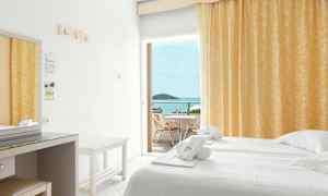 Hotelværelse med en dobbeltseng, hvide lagner og gul gardin. Balkon med bord og stole samt havudsigt. (AI-genereret tekst)