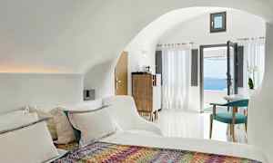 Et lyst og moderne hotelværelse med en seng, farverigt tæppe, siddeområde og store vinduer med udsigt over havet. (AI-genereret tekst)