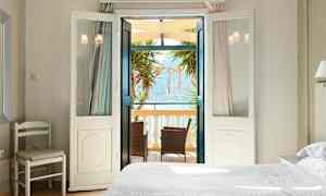 Et lyst soveværelse med åbne døre til en balkon med møbler og udsigt over havet. (AI-genereret tekst)