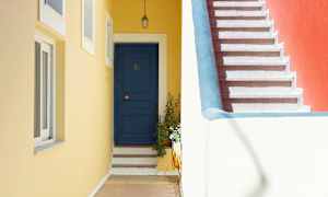 En blå dør med trin og en gul væg ved siden af en trappe med rødt vægparti. (AI-genereret tekst)