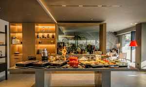 Buffetområde med forskellige retter og drikkevarer på et bord. Baggrund med hylder og siddepladser. (AI-genereret tekst)