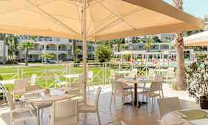 Udendørsrestaurant med møblerede borde nær en pool og omkringliggende bygninger. (AI-genereret tekst)