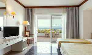 Interiør af et hotelværelse med to senge, skrivebord og en terrasse med udsigt til havet. (AI-genereret tekst)