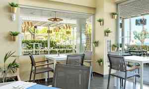 En moderne café med borde og stole, udsigt til grønne træer og udendørsmøbler. (AI-genereret tekst)