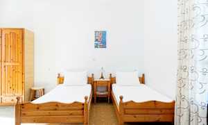 To enkeltsenge med trerammer i et lyst rum med hvide vægge, et lille natbord med lampe imellem dem. (AI-genereret tekst)