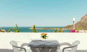 Udsigt over havet fra en balkon med et bord, to stole og en vase med blomster. (AI-genereret tekst)