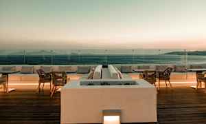 En terrasse med siddepladser og borde med udsigt over havet ved solnedgang. (AI-genereret tekst)