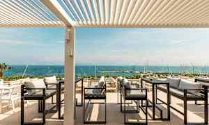 Udendørs servering med udsigt over havet, med sofaer og borde under en pergola. (AI-genereret tekst)