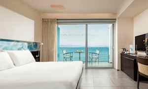 Et hotelværelse med en stor seng, et skrivebord og en balkon med havudsigt. (AI-genereret tekst)