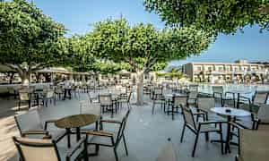 Udendørs område med stole og borde under træer nær en pool. (AI-genereret tekst)