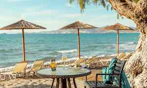 Bord med mad og drikke på en sandstrand med havudsigt og liggestole. (AI-genereret tekst)