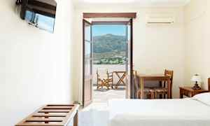 Hotelværelse med åben dør til en balkon med udsigt over bjerge og en landsby. (AI-genereret tekst)