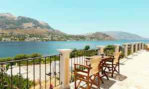 Udsigt fra en terrasse med bord og stole over hav og bjerge. (AI-genereret tekst)