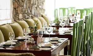 Et bord dækket med glas og tallerkener i en restaurant med grønne stole og grønne puder. (AI-genereret tekst)