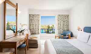 Et hotelværelse med altan, møbler inklusive seng, skrivebord, stol og lænestol. (AI-genereret tekst)