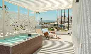 En terrasse med jacuzzi, liggestole og udsigt til palmer og bygninger i baggrunden. (AI-genereret tekst)