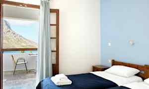 Et værelse med to enkeltsenge og stort vindue med udsigt til en terrasse og en bjergskråning. (AI-genereret tekst)