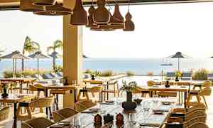 En restaurant med borde og stole, med udsigt over en udendørs pool, havet og parasoller. (AI-genereret tekst)