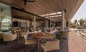 Åbne siddeområder med træborde og flettede stole under et tag. (AI-genereret tekst)