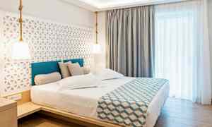 Hotelværelse med en dobbeltseng, stilren indretning og lyse gardiner. (AI-genereret tekst)