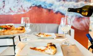 Et bord med pizza og vinglas, baggrund med et billede af stranden. (AI-genereret tekst)