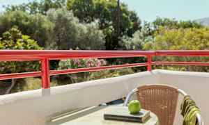 Udsigt fra en altan med rødt gelænder, en møbel med bog og et æble på bordet. (AI-genereret tekst)