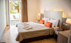 Billede af et hotelværelse med dobbeltseng, to røde puder og et vindue, der fører til en balkon. (AI-genereret tekst)