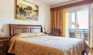 Et hotelværelse med en stor seng, trædetaljer og en balkon med havudsigt. (AI-genereret tekst)