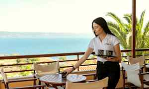 En person placerer genstande på et bord på en udendørs terrasse med havudsigt. (AI-genereret tekst)