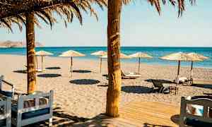 Strand med parasoller og liggestole foran havet. (AI-genereret tekst)