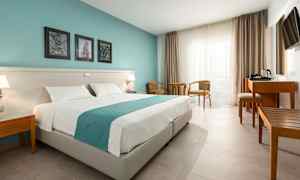 Et hotelværelse med en dobbeltseng, to stole og et bord ved vinduet samt et skrivebord med elkedel. (AI-genereret tekst)