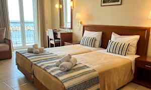 Hotelværelse med to enkeltsenge, skrivebord og udsigt over havet fra altanen. (AI-genereret tekst)