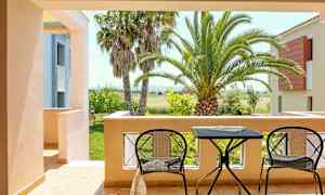 Udsigt fra en terrasse med to stole og et bord, omgivet af palmer og en frodig have. (AI-genereret tekst)