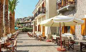 Billede af en gade med palmer, udendørs servering og bygninger med altaner. (AI-genereret tekst)