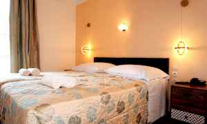 Et soveværelse med to enkeltsenge dækket med et blomstret sengetæppe, hvide puder og rullede håndklæder, samt væglamper. (AI-genereret tekst)