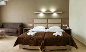 Hotelværelse med to enkeltsenge og en brun sofa. (AI-genereret tekst)