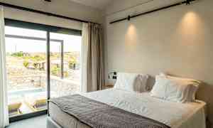 Hotelværelse med stor seng ved et vindue med udsigt til en terrasse med liggestole og en lille pool. (AI-genereret tekst)